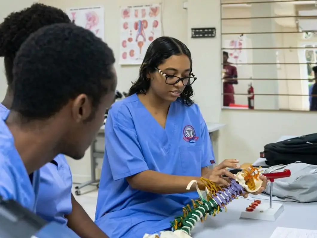 An AAIMS student in scrubs examining a model spine and skull during a small-group anatomy session.